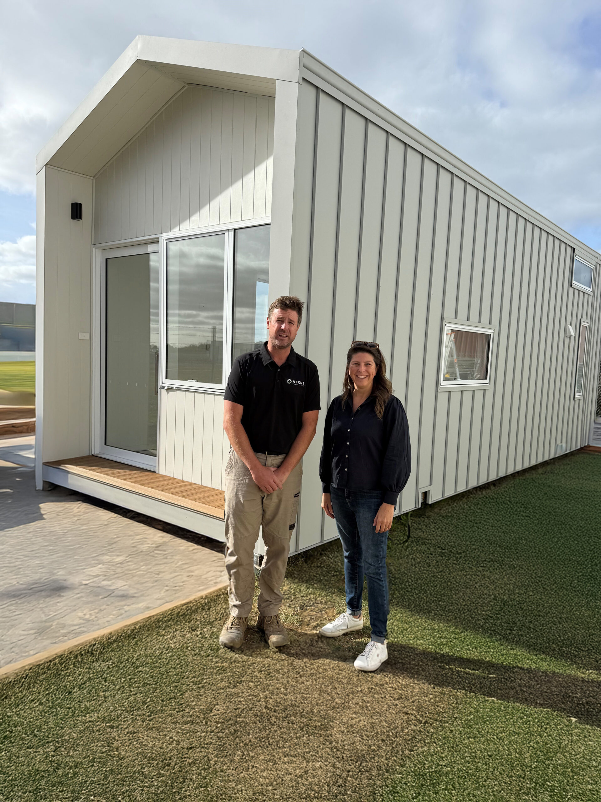 new Tristan Cross and Alison Marchant MP discussing social impact housing in front of a Nexus Communities modular cabin